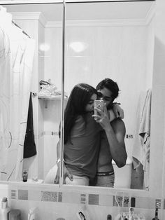 a man and woman standing in front of a bathroom mirror taking a selfie with their cell phone