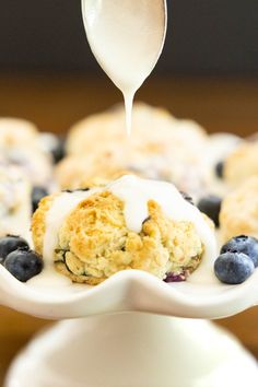 blueberry muffins with icing being drizzled over them on a white plate