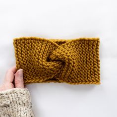 a hand holding up a knitted headband on top of a white tablecloth