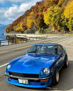 a blue car is parked on the side of the road near some water and trees