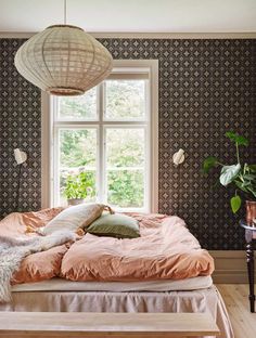 a bed sitting under a window next to a wooden table with pillows on top of it