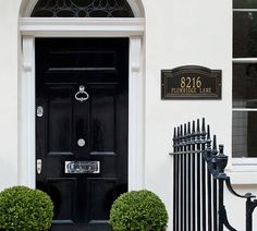 a black door with two potted plants next to it in front of a white building