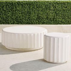 two white tables sitting next to each other on top of a cement slab covered ground