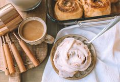 cinnamon rolls on a plate with icing next to baking utensils and coffee