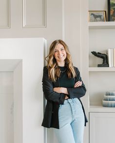 a woman standing in front of a white wall with her arms crossed and looking at the camera