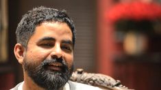 a close up of a person wearing a white shirt and beard with a red flower in the background