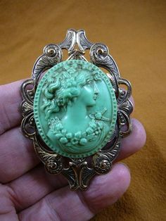 (internal #CL32-6).  You are bidding CAMEO of a WOMAN with HAIR UP, wearing FLOWERS, cameo itself is 1-3/4" long x 1-1/2" wide, organic pine resin cameo has been hand molded from the shell original in BRIGHT MINT GREEN color, antiqued, then mounted on repro Victorian brass; clasp pin/pendant glued horizontally on back.  This is exactly the cameo you would receive. EXCELLENT detail, from the texture of her hair to the superb flowers around her neck and the draping of her gown, HIGH RELIEF.   I kn Victorian Green Collectible Brooches, Antique Green Brooches For Wedding, Vintage Green Flower Brooches, Ornate Green Brooches For Wedding, Green Oval Brooches For Formal Occasions, Pine Resin, Victorian Brass, Mint Green Color, Brass Pin