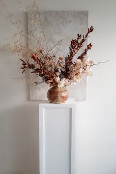 a vase filled with dried flowers sitting on top of a white table next to a painting