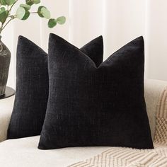 two black pillows sitting on top of a couch next to a vase with a plant