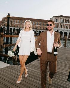 a man and woman are walking on a dock with wine bottles in their hand while holding hands