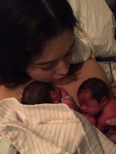 a woman is holding two babies in her arms as they are laying down on the bed