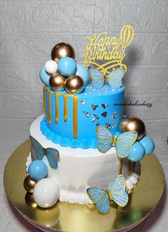 a blue and gold birthday cake with butterflies on the top is sitting on a table