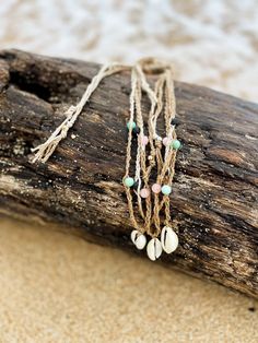 three necklaces with shells on them sitting on top of a piece of driftwood