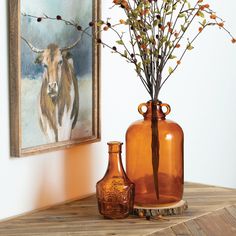 two vases with flowers in them sitting on a table next to a cow painting