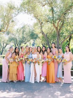 a group of women standing next to each other holding bouquets in front of trees