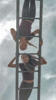 two women standing on a ladder in the air with their legs up and one woman upside down