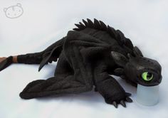 a black dragon doll with green eyes laying on the ground next to a plastic cup