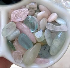 a person holding a white bowl filled with lots of different colored rocks and stones in it