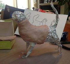 a sculpture of a dog made out of tin foil on a table next to a painting