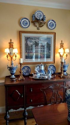 a dining room table with blue and white china on it's sideboard in front of a framed photograph