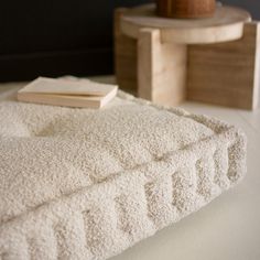 a white blanket on the floor next to a table with a lamp and book sitting on it