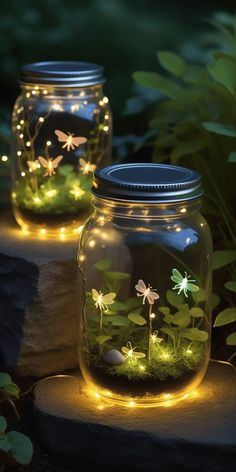 two mason jars with fairy lights in them sitting on the ground next to some plants