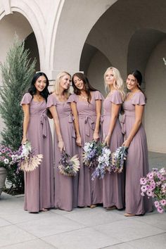 a group of women standing next to each other in long dresses holding bouquets and flowers