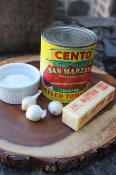 a can of san marzani and some garlic on a wood slice with butter