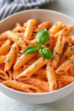 a white bowl filled with pasta covered in sauce and topped with a sprig of basil