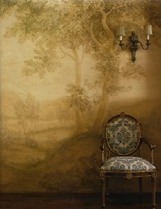 a chair sitting in front of a wall with a painting on it