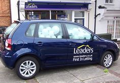 a blue car parked in front of a building with balloons attached to the back window