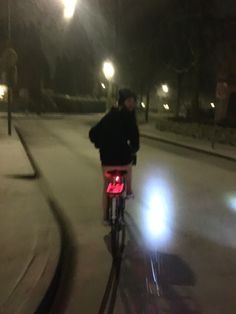 a man riding a bike down a street at night with lights shining on the road