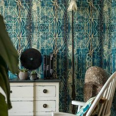 a white chair sitting in front of a wooden dresser next to a green wallpaper