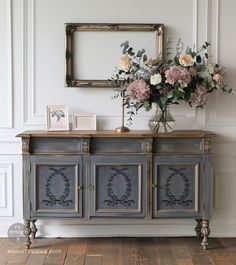 a vase with flowers sitting on top of a blue cabinet next to a mirror and framed photo