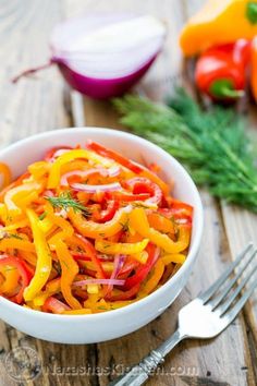 a white bowl filled with red, yellow and green bell peppers next to a knife and fork