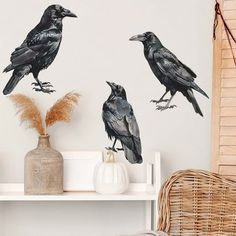 three black birds sitting on top of a white shelf next to a vase with dried flowers