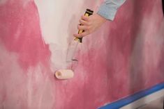 a person using a paint roller to paint a pink and white painting on a wall