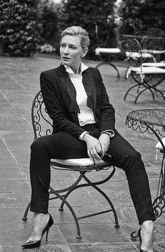 a woman sitting on top of a chair next to a table and chairs in a park