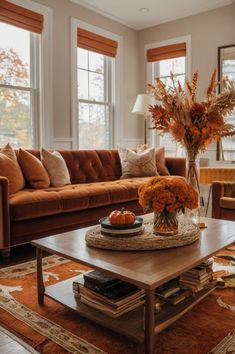 a living room filled with furniture and flowers on top of a coffee table in front of two windows