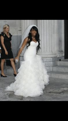 a woman in a white wedding dress is walking down the street with her bridesmaid