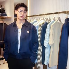 a young man standing in front of a rack of shirts and pants on hangers