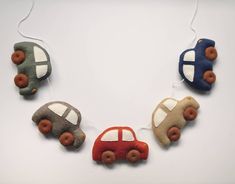 four toy cars are hanging from strings on a white surface, one has donuts in the shape of a car