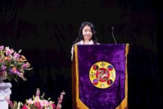 a woman standing at a podium in front of flowers