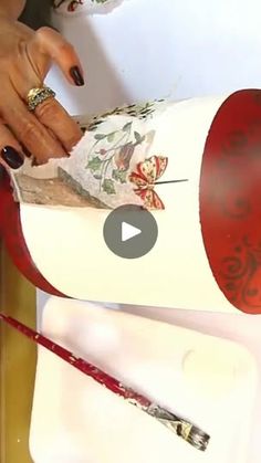 a woman is cutting paper with scissors on top of a white box that has red and green designs