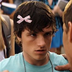 a young man with a pink bow on his head is talking to another person in front of him