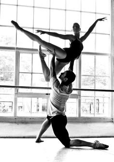 two people are doing acrobatic tricks in an empty room with large windows