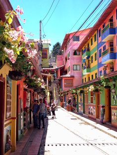 people are walking down the street in front of colorful buildings with flowers growing on them