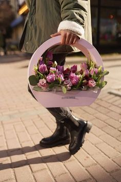 a person holding a pink circle with flowers in it on the sidewalk and wearing black boots