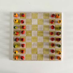 a checker board with small red, yellow and green peppers arranged on the board