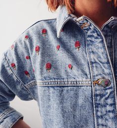 a woman with red hair wearing a denim jacket and pink lipstick on her lips is looking off to the side